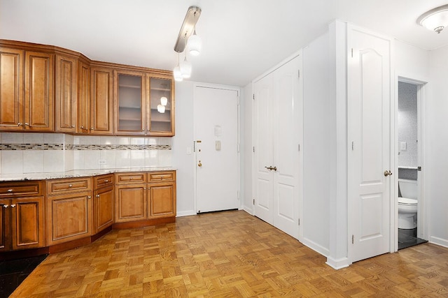 20 W 64th St Unit 11U, New York City, NY 10023 - kitchen with brown cabinets, glass insert cabinets, light stone counters, decorative light fixtures, and decorative backsplash