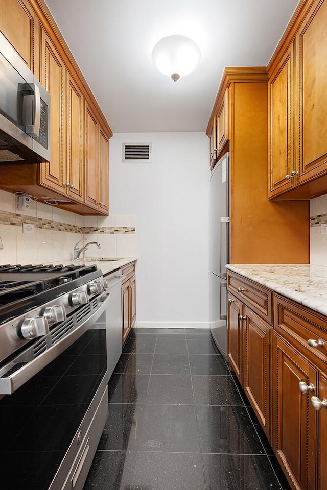 20 W 64th St Unit 11U, New York City, NY 10023 - kitchen with appliances with stainless steel finishes, granite floors, brown cabinetry, backsplash, and light stone countertops
