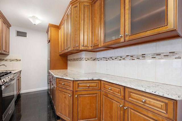 20 W 64th St Unit 11U, New York City, NY 10023 - kitchen with stainless steel range with gas stovetop, brown cabinets, backsplash, light stone counters, and glass insert cabinets