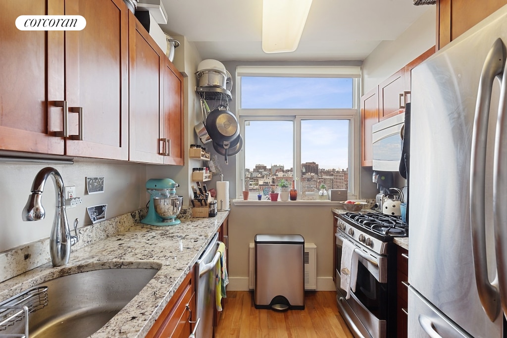 106 W 116th St Unit 10A, New York City, NY 10026 - kitchen with appliances with stainless steel finishes, light wood-type flooring, brown cabinetry, light stone counters, and a city view