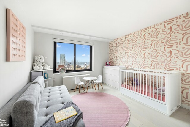 201 W 70th St Unit 24B, New York City, NY 10023 - bedroom featuring wallpapered walls, a crib, an accent wall, and wood finished floors