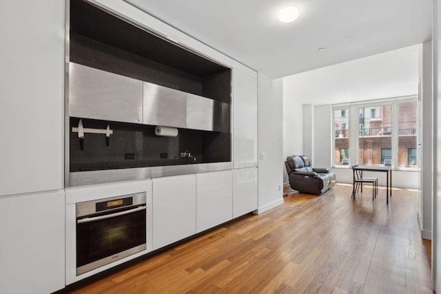 15 William St Unit 9C, New York City, NY 10004 - kitchen with stainless steel oven, white cabinetry, light wood finished floors, modern cabinets, and light countertops
