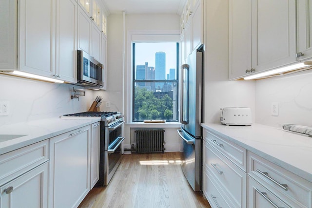 350 W 48th St Unit 4E, New York City, NY 10036 - kitchen featuring stainless steel appliances, radiator, light wood finished floors, and white cabinetry