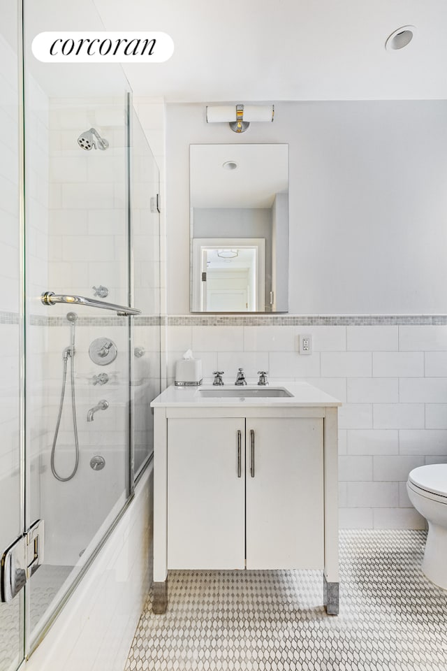 174 W 76th St Unit 3H, New York City, NY 10023 - full bathroom featuring tile walls, vanity, bath / shower combo with glass door, tile patterned flooring, and wainscoting