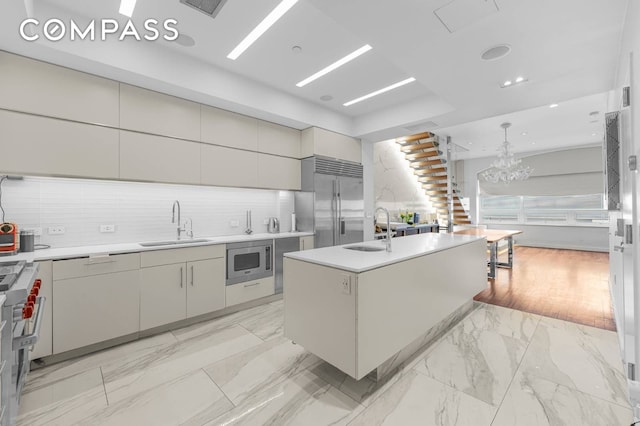 124 E 13th St Unit 3, New York City, NY 10003 - kitchen featuring built in appliances, decorative backsplash, light countertops, light marble finish floors, and a kitchen island with sink