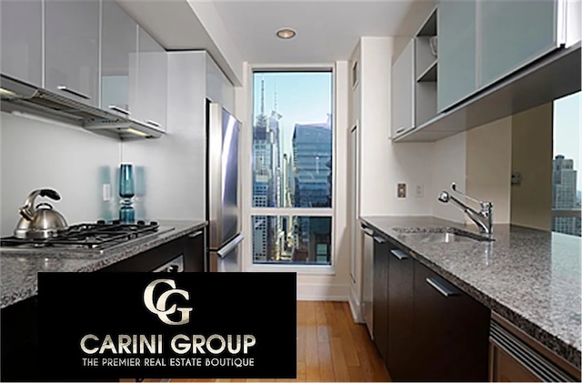 350 W 42nd St Unit 46E, New York City, NY 10036 - kitchen featuring appliances with stainless steel finishes, light wood-style flooring, a view of skyline, dark stone counters, and recessed lighting
