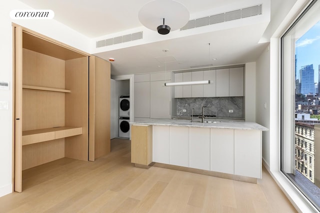 250 E 25th St Unit 9D, New York City, NY 10010 - kitchen featuring estacked washer and dryer, modern cabinets, decorative backsplash, light wood-style flooring, and light stone counters