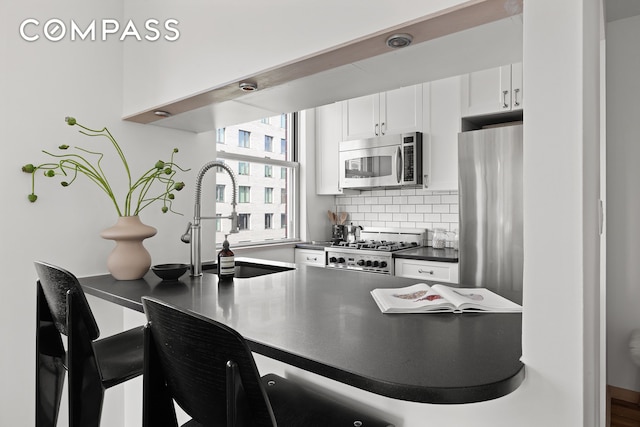 350 W 14th St Unit 6D, New York City, NY 10014 - kitchen with appliances with stainless steel finishes, dark countertops, white cabinets, tasteful backsplash, and a kitchen breakfast bar