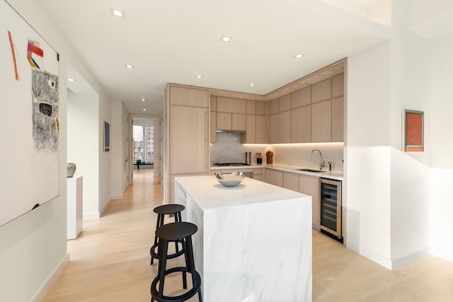 138 E 50th St Unit 26A, New York City, NY 10022 - kitchen with beverage cooler, stainless steel gas stovetop, light countertops, light wood finished floors, and light brown cabinets