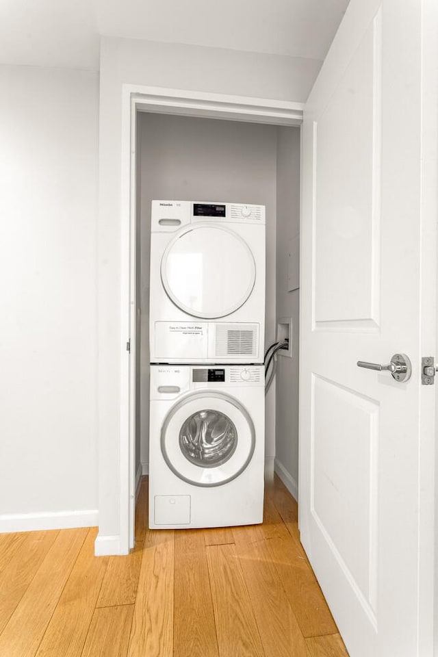 20 W St Unit 18F, New York City, NY 10004 - washroom featuring stacked washer / dryer and light wood-style flooring