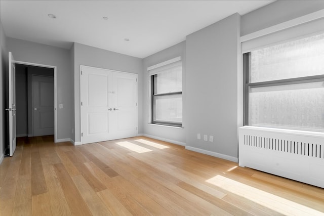 20 W St Unit 18F, New York City, NY 10004 - unfurnished bedroom featuring multiple windows, light wood-style flooring, radiator heating unit, and a closet