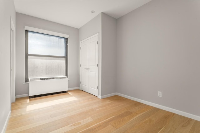 20 W St Unit 18F, New York City, NY 10004 - unfurnished bedroom featuring light wood-style flooring, radiator heating unit, and a closet