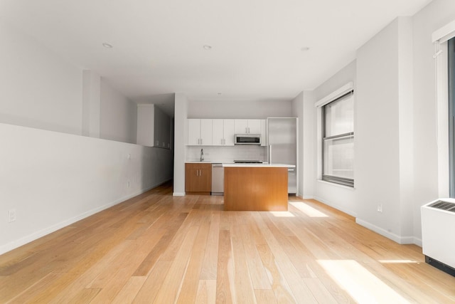 20 W St Unit 18F, New York City, NY 10004 - kitchen featuring appliances with stainless steel finishes, light wood-style flooring, light countertops, white cabinetry, and open floor plan