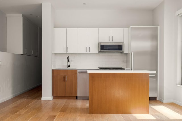 20 W St Unit 18F, New York City, NY 10004 - kitchen with appliances with stainless steel finishes, light wood-style floors, light countertops, backsplash, and white cabinets