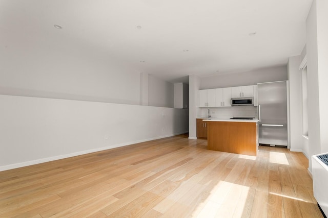 20 W St Unit 18F, New York City, NY 10004 - kitchen with stainless steel appliances, a kitchen island, open floor plan, white cabinetry, and light wood-style flooring