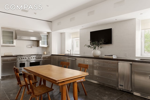 950 5th Ave Unit 3/4, New York City, NY 10075 - kitchen with appliances with stainless steel finishes, wall chimney range hood, tasteful backsplash, glass insert cabinets, and dark countertops