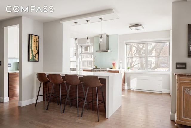70 E 10th St Unit 3B, New York City, NY 10003 - kitchen with wall chimney range hood, a breakfast bar, light wood-style floors, light countertops, and decorative light fixtures