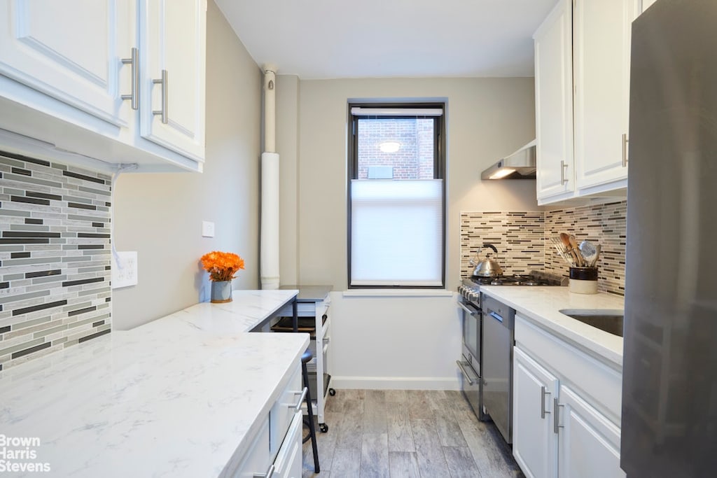 221 E 78th St Unit 6F, New York City, NY 10075 - kitchen featuring appliances with stainless steel finishes, white cabinets, backsplash, light wood-style floors, and light stone countertops