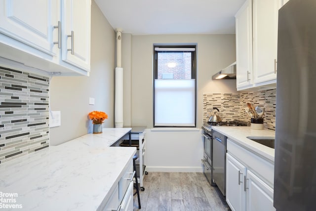 221 E 78th St Unit 6F, New York City, NY 10075 - kitchen featuring appliances with stainless steel finishes, white cabinets, backsplash, light wood-style floors, and light stone countertops