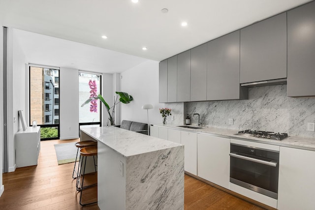 287 E Houston St Unit 4B, New York City, NY 10002 - kitchen featuring stainless steel appliances, a kitchen island, light wood finished floors, decorative backsplash, and gray cabinetry