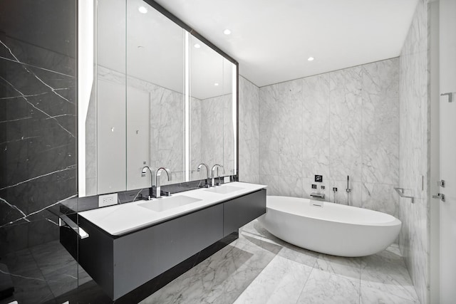 520 W 28th St Unit 7, New York City, NY 10001 - bathroom with tile walls, a soaking tub, marble tiled floors, double vanity, and recessed lighting