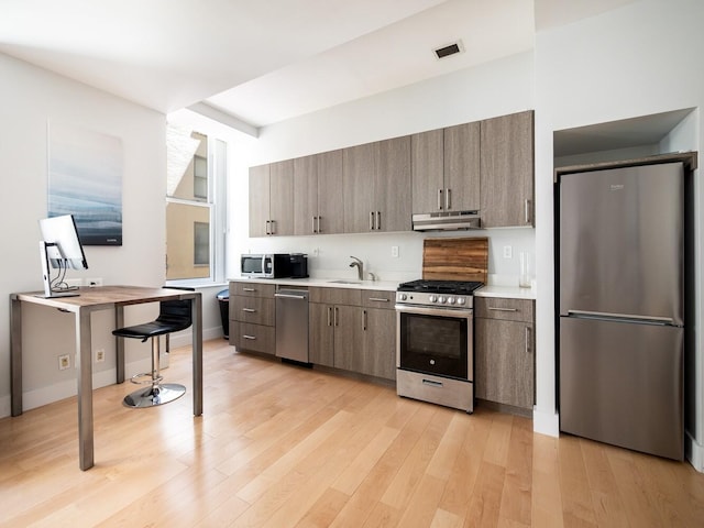 55 Wall St Unit 713, New York City, NY 10005 - kitchen featuring appliances with stainless steel finishes, under cabinet range hood, light countertops, and light wood-style flooring