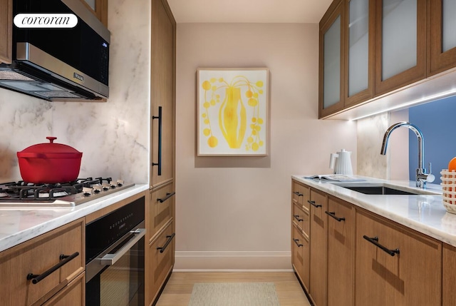 210 Warren St Unit 9B, New York City, NY 10282 - kitchen with appliances with stainless steel finishes, light wood-style flooring, brown cabinets, glass insert cabinets, and light stone countertops
