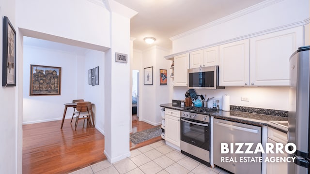 259 Bennett Ave Unit 2F, New York City, NY 10040 - kitchen with stainless steel appliances, white cabinets, light tile patterned flooring, dark stone counters, and ornamental molding