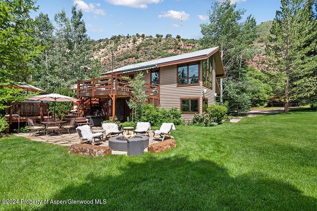 back of property featuring a lawn, a patio area, a deck, and an outdoor fire pit