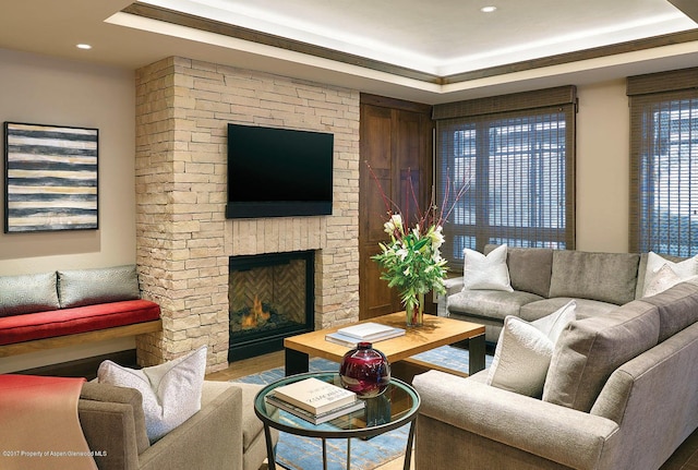 living room featuring wood finished floors, a raised ceiling, recessed lighting, and a stone fireplace