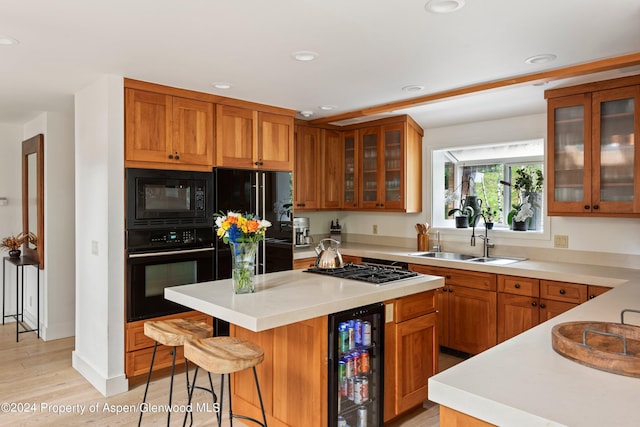 kitchen with sink, beverage cooler, a kitchen bar, a kitchen island, and black appliances