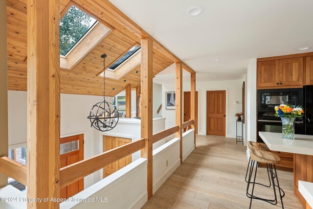 corridor with light hardwood / wood-style flooring, lofted ceiling with skylight, wooden ceiling, and a notable chandelier