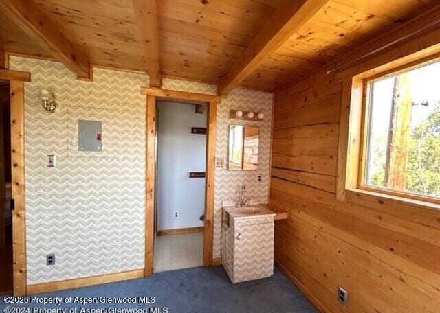 carpeted empty room featuring wooden walls, beam ceiling, and wooden ceiling
