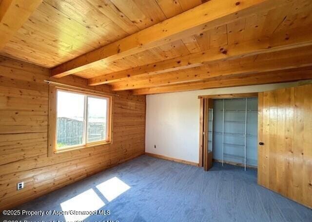 unfurnished bedroom with wooden walls, carpet, wooden ceiling, baseboards, and beam ceiling
