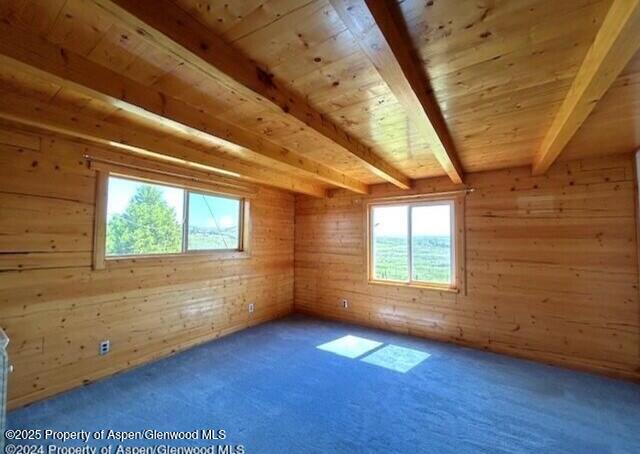 spare room with beamed ceiling, wood walls, carpet floors, and wood ceiling