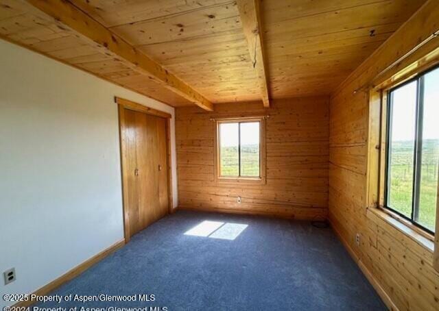 carpeted spare room with beamed ceiling, wooden walls, and wood ceiling