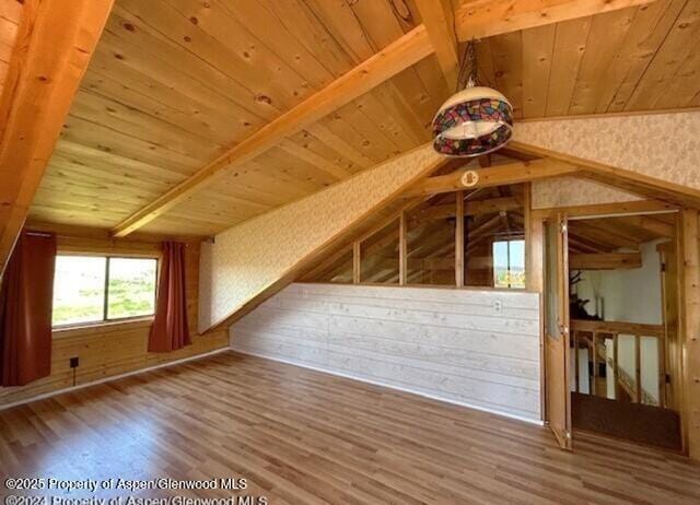 bonus room with wooden ceiling, wood walls, lofted ceiling with beams, and wood finished floors