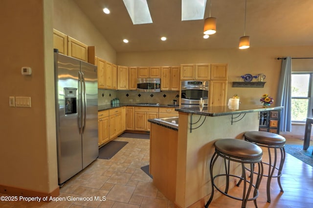 kitchen with decorative backsplash, light brown cabinetry, appliances with stainless steel finishes, dark countertops, and a breakfast bar