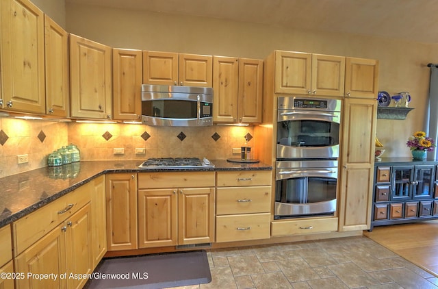 kitchen with decorative backsplash, dark stone countertops, appliances with stainless steel finishes, and light brown cabinetry