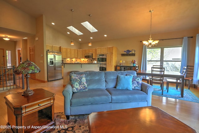 living area featuring a skylight, high vaulted ceiling, a chandelier, light wood-style floors, and recessed lighting