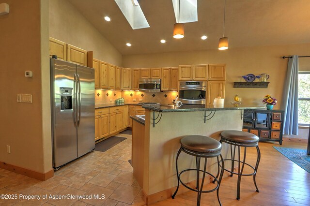 kitchen featuring baseboards, appliances with stainless steel finishes, light brown cabinets, and a skylight