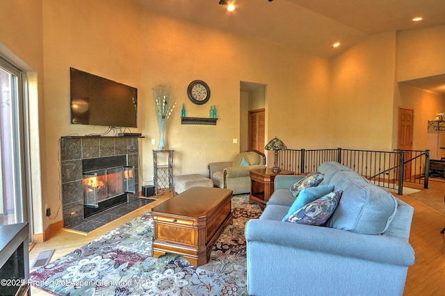 living room featuring a tiled fireplace, high vaulted ceiling, wood finished floors, and visible vents