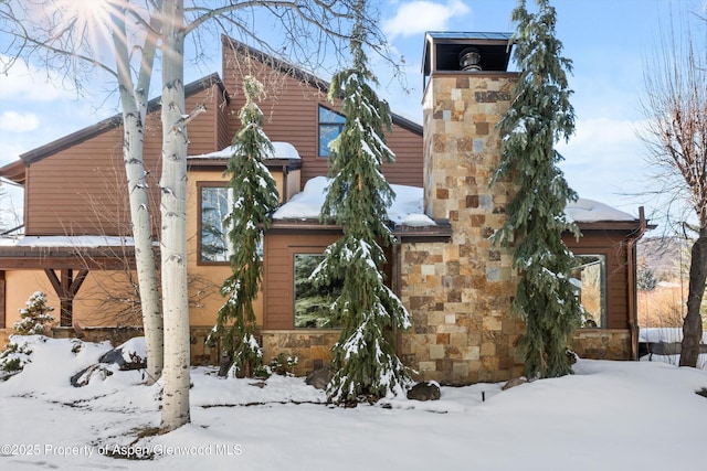 view of snow covered exterior featuring stone siding and a chimney