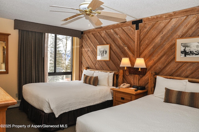 bedroom featuring ceiling fan, a textured ceiling, and wood walls