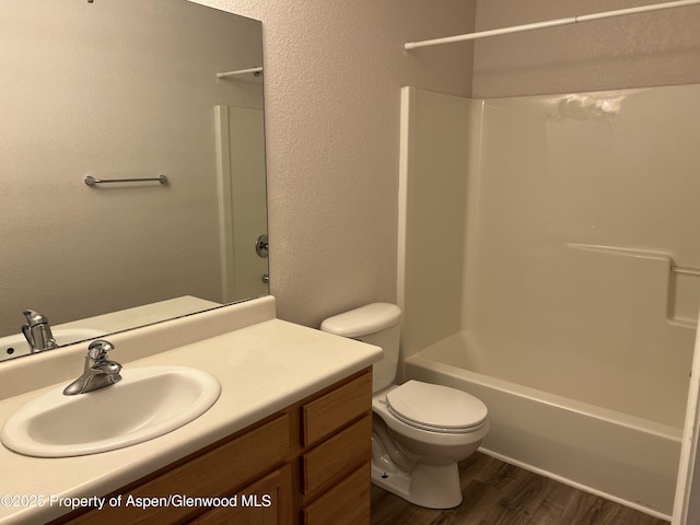 full bath with a textured wall, toilet, wood finished floors, vanity, and bathing tub / shower combination