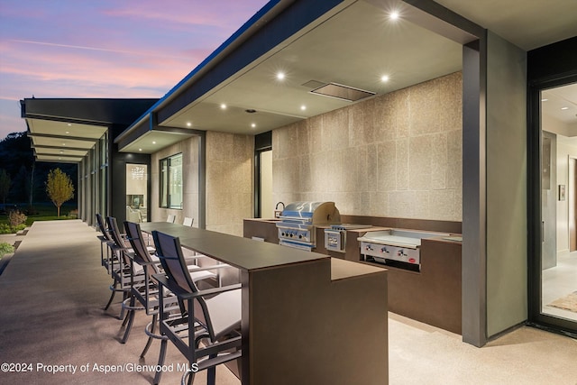 patio terrace at dusk featuring area for grilling, exterior kitchen, and exterior bar