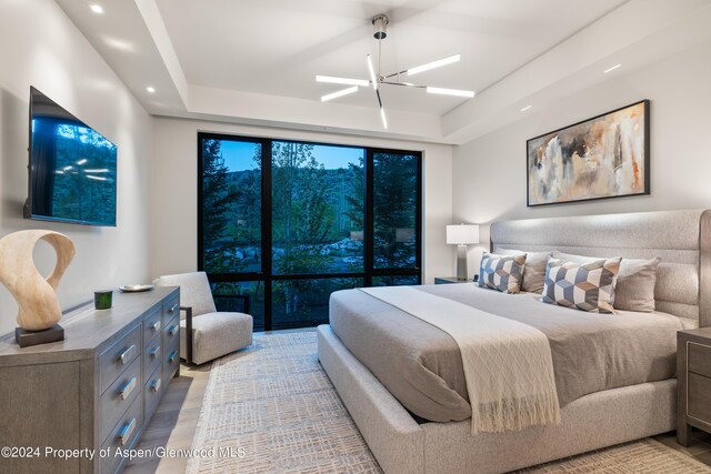 bedroom featuring ceiling fan with notable chandelier, a tray ceiling, and light hardwood / wood-style flooring