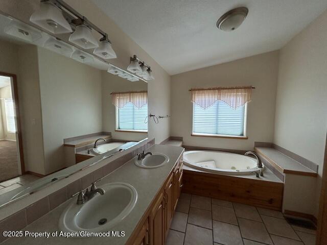 bathroom featuring a sink, tile patterned flooring, a jetted tub, and lofted ceiling