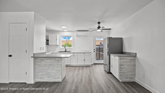 2430 W Ave, Rifle, CO 81650 - kitchen featuring freestanding refrigerator, white cabinetry, a wall unit AC, light wood-style floors, and a peninsula