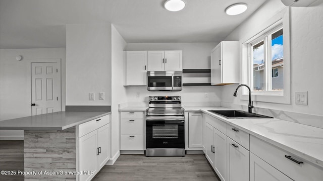 2430 W Ave, Rifle, CO 81650 - kitchen featuring stainless steel appliances, a peninsula, white cabinetry, wood finished floors, and light stone countertops